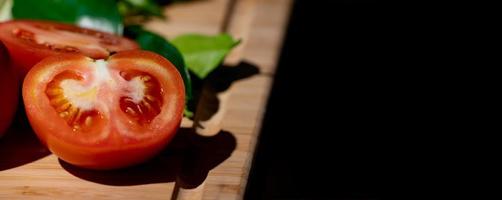 tomate e metade do tomate fatiado ao lado, na placa de madeira na luz do estúdio com tema escuro. foto