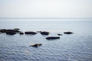 paisagem marítima em tons de azul com pedras na água barcos podem ser vistos no horizonte, e um caranguejo está sentado nas rochas foto