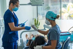 dentista feminina com um assistente examina um paciente na clínica odontológica. foto