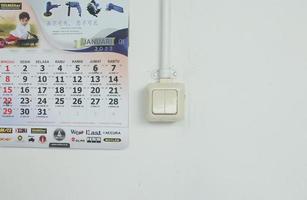 jacarta, indonésia - 27 de janeiro de 2023 - interruptor de lâmpada de parede branco simples e calendário de enforcamento de janeiro em bahasa indonésia isolado na parede vazia foto
