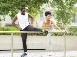 jovem família afro-americana tenta fazer alongamento depois de correr ao ar livre no parque. casal alegre exercitando como atividade de lazer. marido e mulher recreação juntos estilo de vida saudável. foto