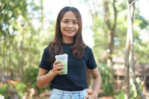 mulher asiática feliz bebendo chá verde em um fundo de café com árvores verdes foto