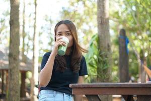 mulher asiática feliz bebendo chá verde em um fundo de café com árvores verdes foto