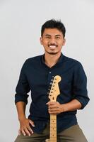 retrato de jovem asiático na camisa azul com guitarra eletrônica isolada no fundo branco foto