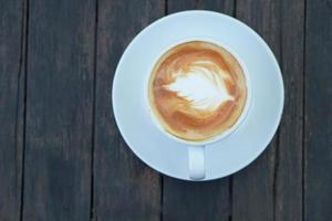 café quente com espuma floral em um copo branco fundo de madeira cinza foto