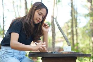 as mulheres asiáticas ficam felizes em sentar e trabalhar em uma cafeteria. há árvores verdes cercadas pela natureza. planejamento de negócios é uma boa ideia. foto