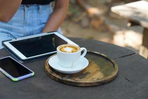 café quente em mãos humanas. flores de espuma de café em uma xícara branca. fundo de madeira cinza foto