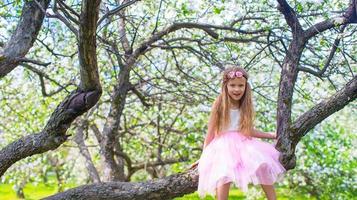 menina adorável sentada na árvore florescendo no jardim de maçã foto