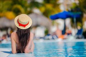 bela jovem relaxante na piscina. vista traseira da garota na piscina ao ar livre no hotel de luxo foto