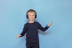 menino em fones de ouvido, ouvindo música e dançando em um fundo azul foto