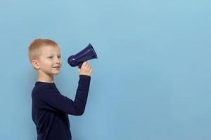 menino com um olhar sonhador fala em um megafone em um fundo azul com espaço de cópia foto