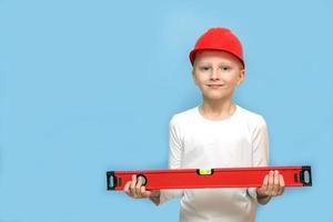 menino em um capacete protetor mantém um nível de construção em suas mãos sobre um fundo azul com espaço de cópia foto