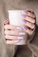 as mãos da menina com delicada manicure roxa segurando uma xícara de chá. foto