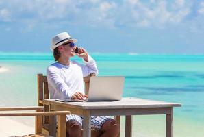 jovem com computador tablet e celular na praia tropical foto