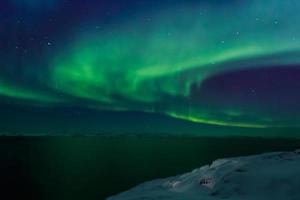 aurora boreal verde em espiral brilhando sobre o fiorde com montanhas ao fundo, nuuk, groenlândia foto