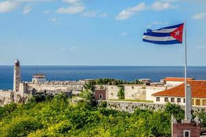 el morro fortaleza espanhola com farol, canhões e bandeira cubana em primeiro plano, com o mar ao fundo, havana, cuba foto