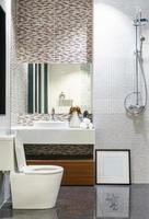 banheiro moderno e espaçoso com azulejos brilhantes com box de vidro, toalete e pia. vista lateral foto