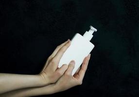 mãos femininas segurando um frasco de loção branca foto