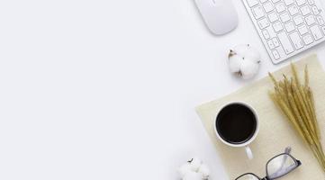 Vista superior da mesa de mesa de escritório mínima com teclado de computador, mouse, óculos, planta de arroz de xícara de café, saco em uma mesa branca com espaço de cópia, composição de local de trabalho de cor branca, postura plana foto