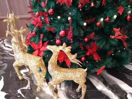 a árvore de natal é decorada com laços vermelhos e laços vermelhos e é cercada por renas douradas cintilantes foto