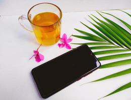 uma xícara de chá, telefone de mão e fundo branco isolado de folha de palmeira pela manhã parecem relaxantes foto