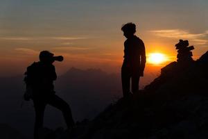 fotógrafo realiza fotografia para uma garota ao pôr do sol em altas montanhas em silhuetas foto