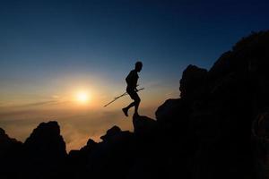 silhueta do pôr do sol do homem skyrunner escalando o cume alpino com bastões foto