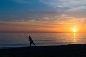 pescador com vara de pescar faz o lançamento no mar foto