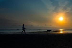 mulher caminhando na praia para o mar com seu cachorro foto