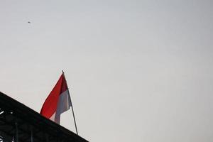 o mastro de bandeira vermelho e branco indonésio tremula contra um fundo de céu nublado foto