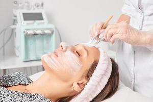 cosmetologista aplicando máscara de creme cosmético no rosto de mulher para rejuvenescimento, procedimento em salão de beleza foto