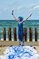 artista performática mulher feliz em vestido azul manchado com tintas guache azul dançando na praia foto