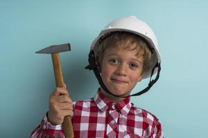 um menino bonito em um capacete de construção com um martelo na mão, um retrato de um pequeno construtor em um capacete foto