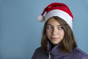 uma linda garota em um st. chapéu de nicholas e uma jaqueta quente sobre um fundo azul está sonhando, ano novo, natal, presentes foto