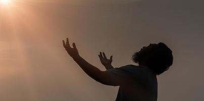 adoração com fé do conceito cristão. a oração espiritual entrega a luz do sol com um lindo fundo desfocado do nascer do sol. pregador reza a Deus pela manhã com devoção. homem cristão tem esperança. foto