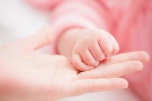 feche a mãe de mãos dadas menina recém-nascida em um quarto. bebê adorável repousa sobre lençóis brancos, olhando para a câmera parecendo pacífico. infância, saúde e pediatria, conceito de infância. foto