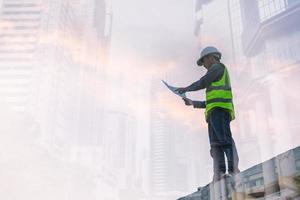 imagem de dupla exposição de engenheiro civil e trabalhador da construção civil com capacete de segurança e desenho de construção no contexto do canteiro de obras surreal na cidade noturna ou paisagem urbana escura. foto