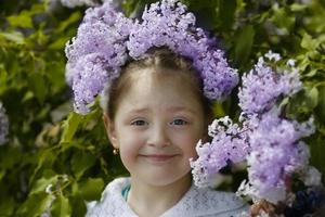 bielorrússia, cidade de gomil, 16 de maio de 2016. rua da cidade. uma linda garotinha fica perto de um arbusto lilás e sorri. foto