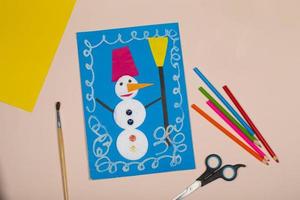 artesanato de papel de natal infantil. aplicação da criatividade das crianças. jardim de infância e escola de artesanato. sobre um fundo bege, um boneco de neve feito de papel colorido. foto