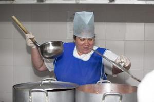 uma mulher cozinha em uma cozinha industrial com uma grande concha entre panelas de metal. cozinheiro do hospital foto