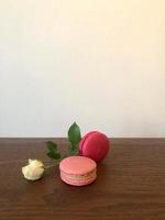 rosa branca e dois biscoitos rosa na mesa de madeira, espaço para exibição vertical de texto foto