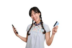 retrato da bela jovem mulher asiática feliz em vestido jeans segurando o cartão de crédito e smartphone em fundo branco. foto de estúdio