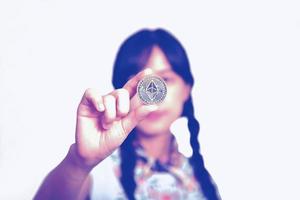 retrato da bela jovem mulher asiática feliz em vestido jeans segurando moeda de moeda criptográfica em fundo branco. foto