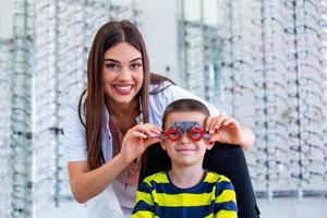 oftalmologista atraente examinando o menino jovem com quadro de teste de optometrista. criança paciente para verificar a visão na clínica oftalmológica foto