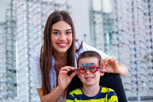 oftalmologista atraente examinando o menino jovem com quadro de teste de optometrista. criança paciente para verificar a visão na clínica oftalmológica foto