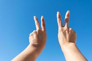 mãos de mulher mostrando sinal de vitóriamãos de mulher mostrando sinal de vitória contra o fundo do céu azul, foto