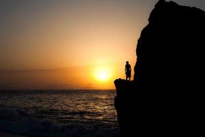 homem em uma rocha ao pôr do sol no mar foto