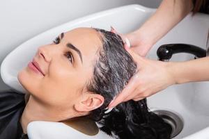 cabeleireiro profissional lavando cabelo de jovem no salão de beleza foto