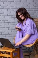 linda empresária trabalhando em um laptop em uma cadeira perto da janela. freelancer feminino conectando-se à internet via computador. blogueiro ou jornalista escrevendo novo artigo. foto
