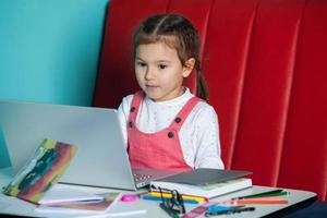 menina bonitinha usando laptop em casa. de volta ao conceito de escola. a garota faz a lição de casa sozinha no laptop foto